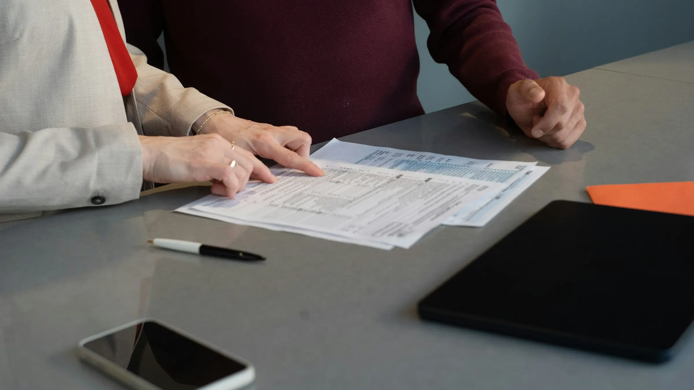 Dos personas revisando unos documentos a un lado y otro de la mesa de una asesoría